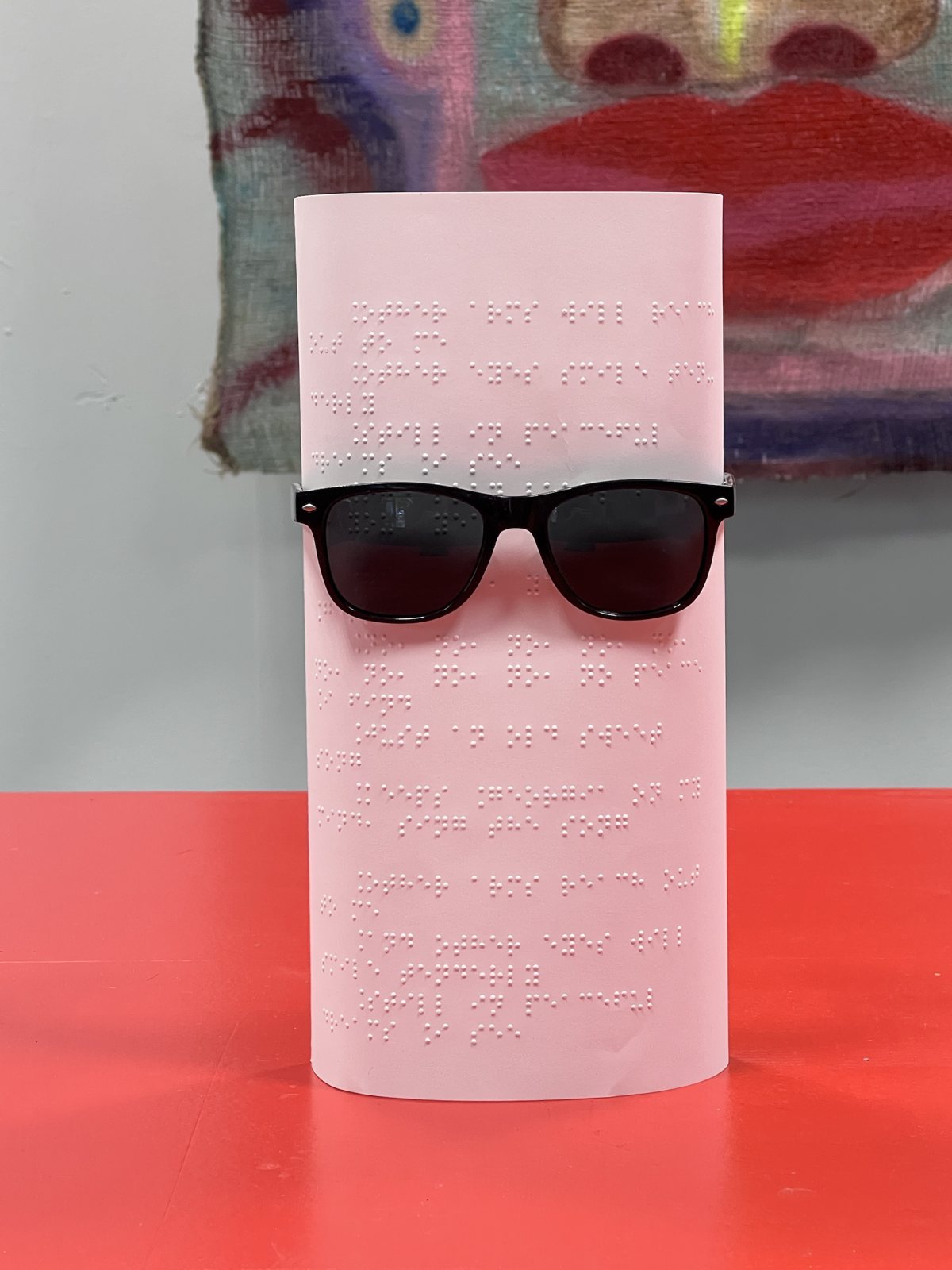 Pink braille sheet wearing black sunglasses on the red table